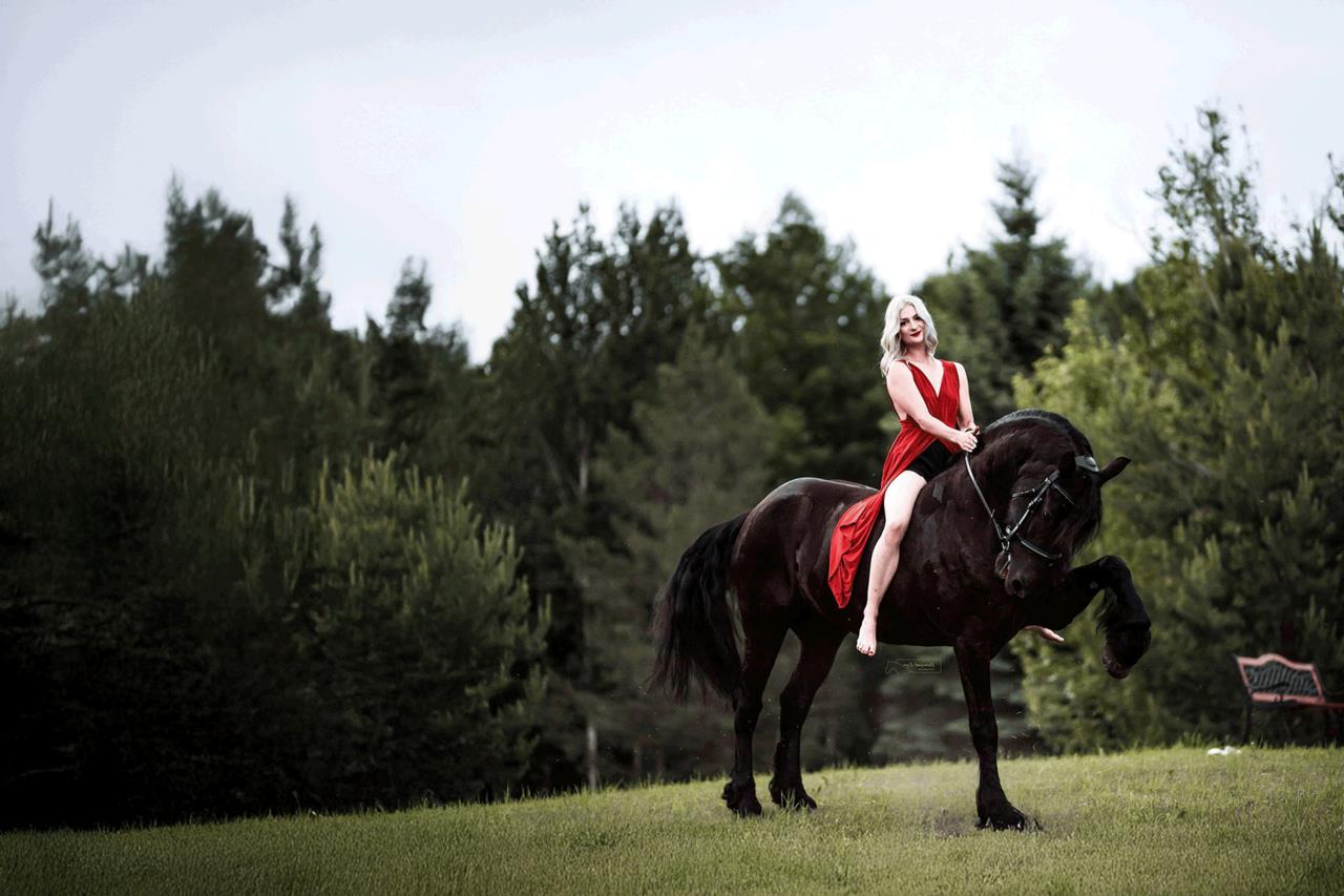 A young woman in a flowing red dress rides a graceful horse across a sunlit pasture at Excella Equine Park, showcasing the harmony between rider and horse.